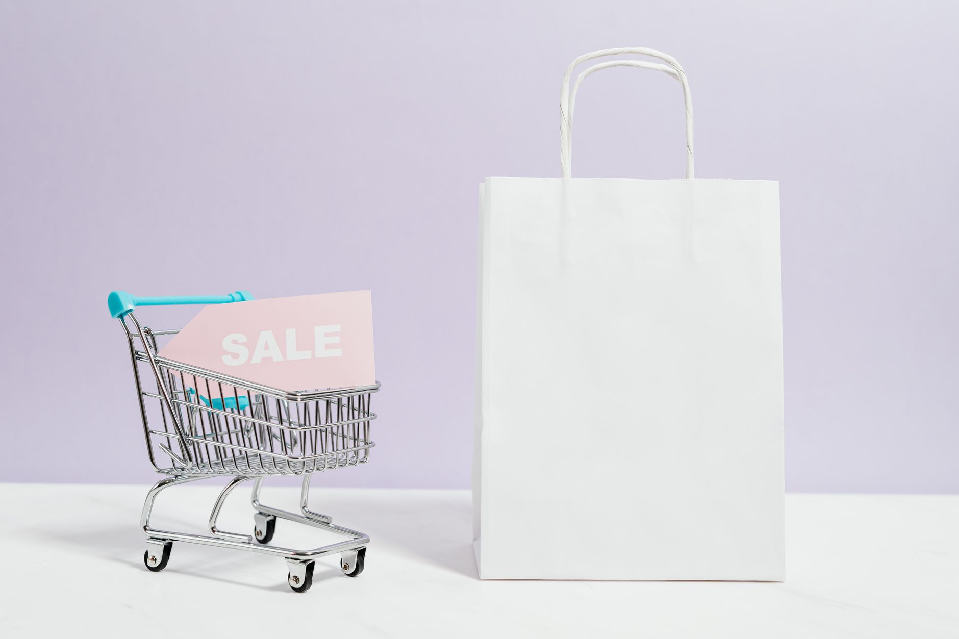 Miniaturowy wózek z napisem sale obok papierowej torby zakupowej