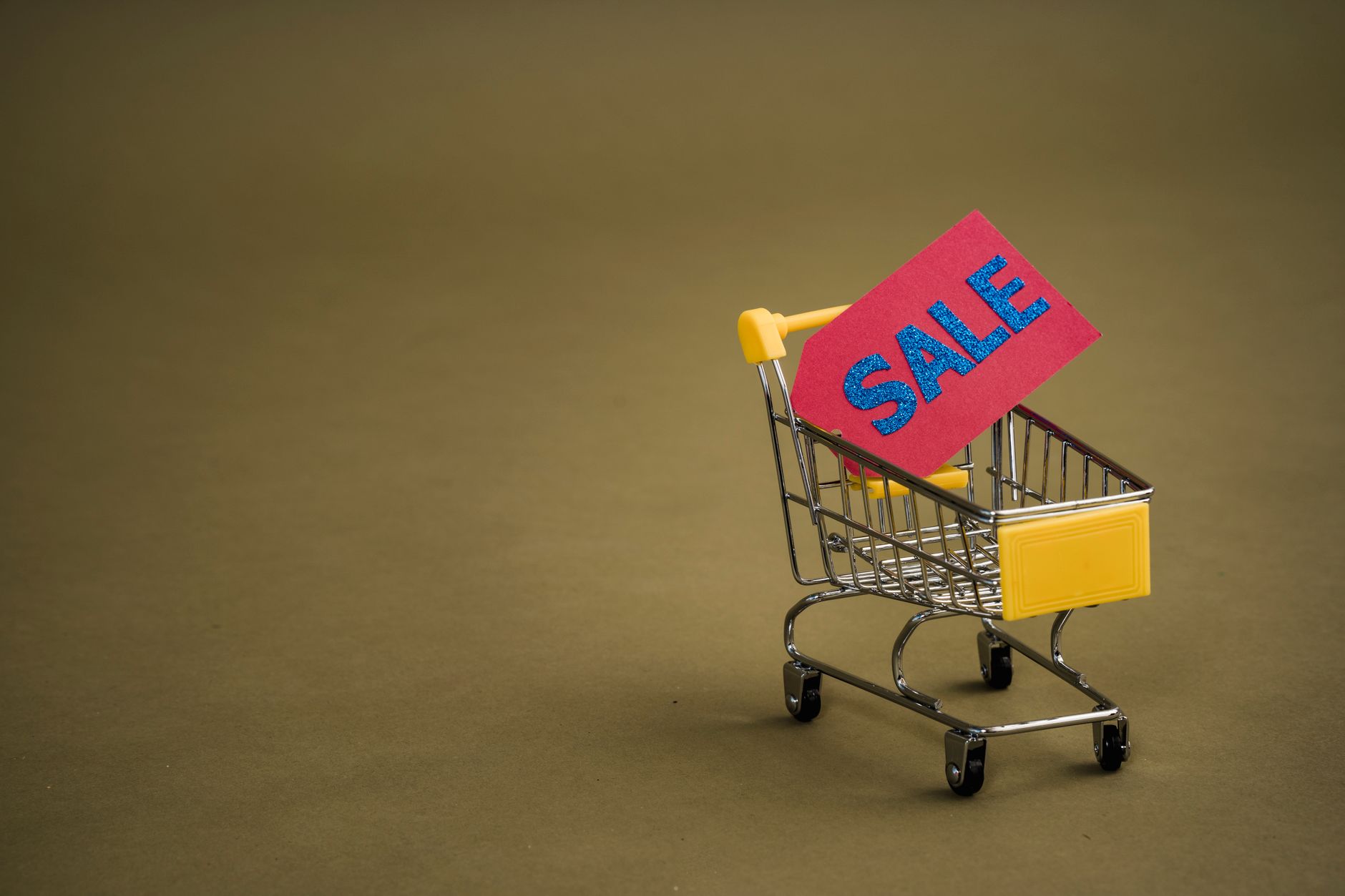 Miniaturowy wózek zakupowy z czerwoną metką SALE na brązowym tle