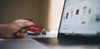 Osoba trzyma kartę płatniczą podczas zakupów online na laptopie