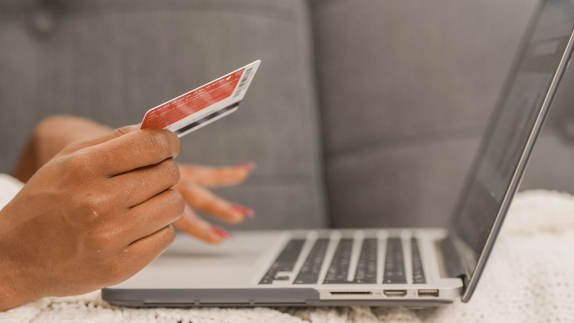Zbliżenie dłoni płacącej kartą przy zakupach online na laptopie